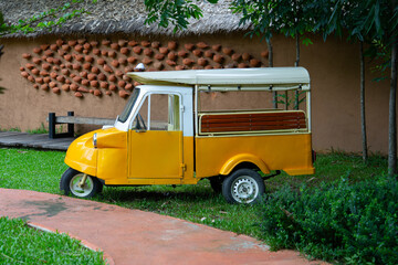 Vintage yellow tuk tuk parked on grass near rustic wall, evoking nostalgic and charming atmosphere