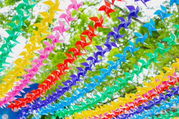 Colorful paper pinwheels hang in rows against green leafy background, creating vibrant and festive atmosphere