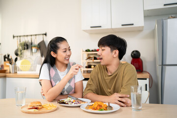 Asian young couple husband and wife eat food on dinner table in house.