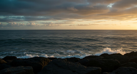 Dramatic seascape with dark rocks, crashing waves, and a golden sunset sky
