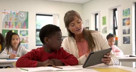 Teacher using tablet helping student with schoolwork in classroom, focused learning - Powered by Adobe