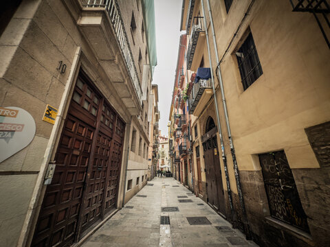 BARCELONA, SPAIN - APRIL 12, 2025: Narrow pedestrian alley in Barcelona El Raval district, flanked by historic buildings with balconies, worn stone pavement, capturing the character of Ciutat Vella.