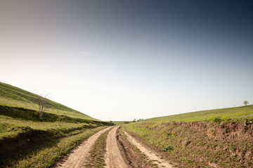 Unpaved dirt path winding between green hills at Titelski Breg in Vojvodina, Serbia, under a wide...