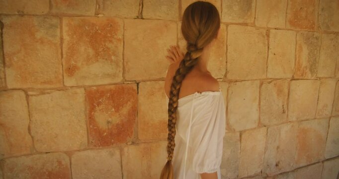 Woman walking inside Mayan temple touching stone wall at archaeological ruins