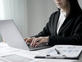 Young Asian business woman sitting at the table holding a pen, recording investments and planning...