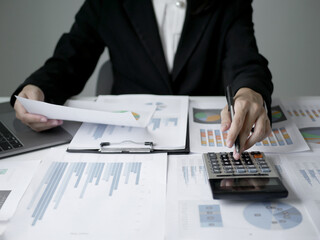 Young Asian business woman sitting at the table holding a pen, recording investments and planning...