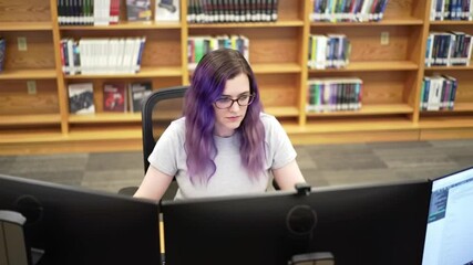 Woman with violet hair coding on multiple displays in a library setting - Powered by Adobe