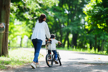 自転車の練習をする5歳の男の子とフォローする母親