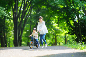 Obraz premium 自転車の練習をする5歳の男の子とフォローする母親