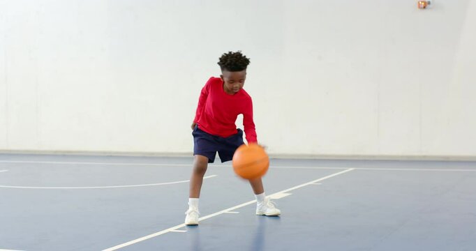 Practicing basketball dribbling, african american boy focused on indoor court, copy space