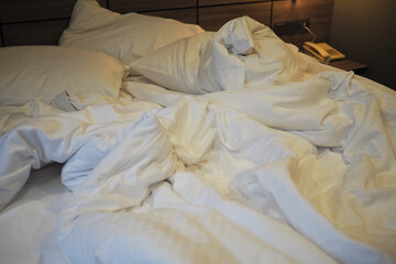 Messy bed with white sheets in a cozy hotel room