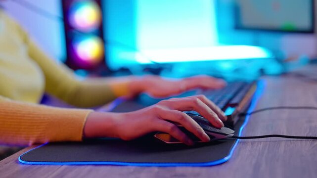 Close-up of hands on gaming mouse and keyboard with illuminated RGB mouse pad, young gamer immersed in eSports or streaming session in colorful setup with neon blue lighting and modern desktop gear.