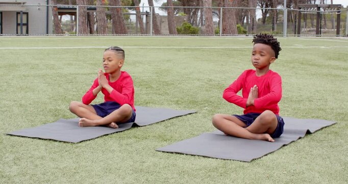 multiracial boys practicing yoga on mats on school field, focusing and relaxing