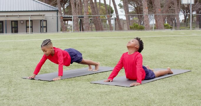 Multiracial boys practicing yoga on mats on school field, enjoying exercise and fresh air