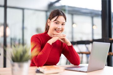 Young beautiful joyful woman in red sweater smiling while working with laptop