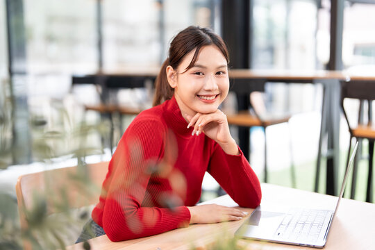Young beautiful joyful woman in red sweater smiling while working with laptop
