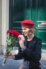 Beautiful young woman wearing military red beret is excited about bouquet of red roses she have got as romantic present, while sitting on stairs in Amsterdam , Nederland.