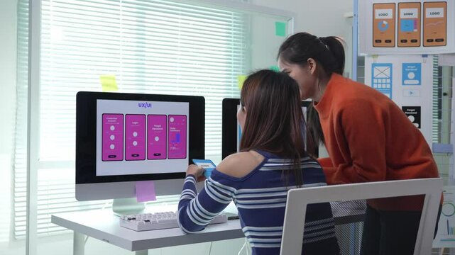 Young professional web designers collaborating on mobile application user interface, analyzing design elements and testing user experience in modern office environment