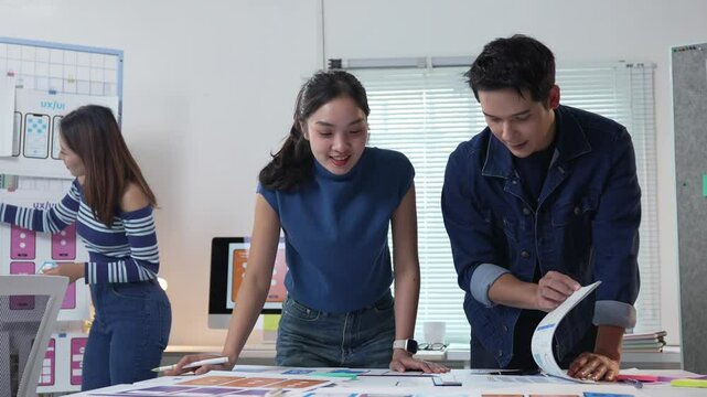 Professional UX designers collaborating on mobile application prototype, drawing wireframes and sharing creative ideas in bright, modern startup office environment