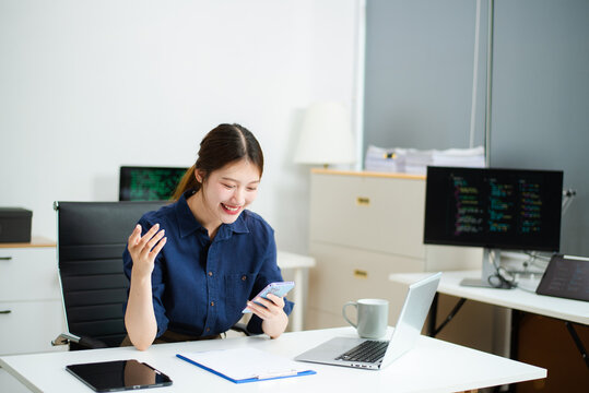 Young Asian female developer working on code with laptop and dual screens in a bright office. Ideal for themes of women in tech, programming