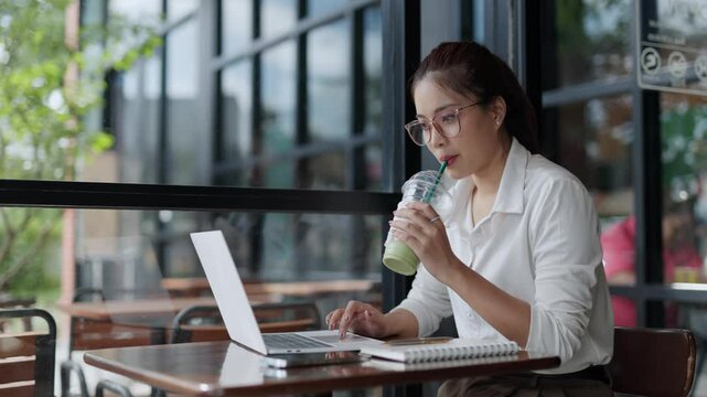 Professional businesswoman enjoying matcha latte while working on laptop, blending productivity and relaxation in contemporary urban cafe setting