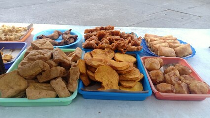 An assortment of Indonesian fried snacks sold by a street vendor, including fried tofu, tempeh, cassava, bakwan (vegetable fritters), and banana fritters. Crispy, savory, and popular as affordable 
