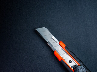 Close-up of a sharp utility cutter with ergonomic design, placed on a dark textured background for...