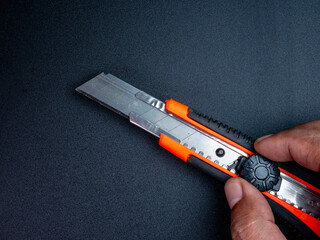 Hand turning metal cutter lock with orange-black handle on black background, showing how to use cutting tool safely and precisely.