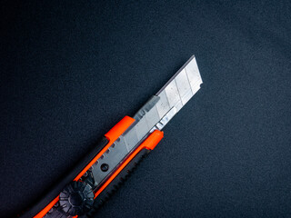A metal cutter knife with orange and black grip placed on a smooth black surface. Ideal for office, industrial, or design purposes.