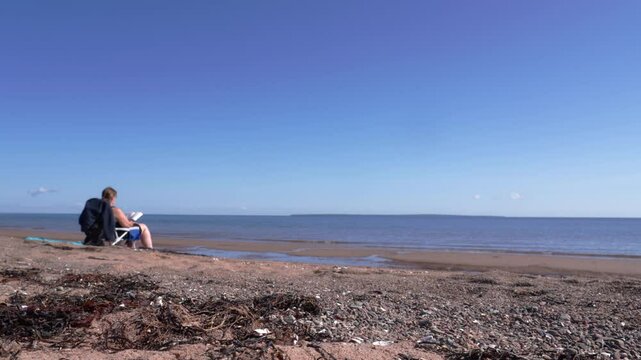 Relaxing day by the ocean with woman sitting on the beach near dry seaweed