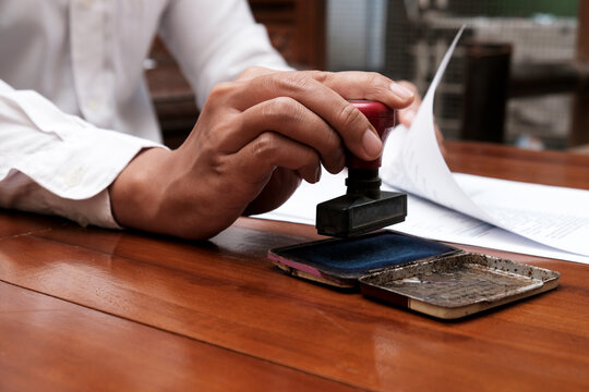 Close-up Of  A man hand holding stamp and document approved certified contract law and paperwork permit, on table in workplace