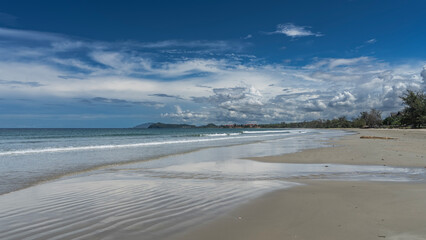 Beautiful tropical beach. A sunny day. The waves of the turquoise ocean spread over the wet sand. Mountains in the distance. Blue sky, clouds. Malaysia. Borneo. Kota Kinabalu.