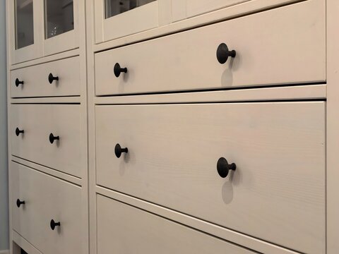 Close-up of modern white wooden drawers with black knobs