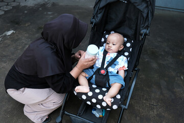 Young woman muslim with a cute baby boy in baby stroller at outdoor in the morning, happy family