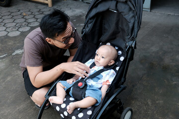 A southeast asian man with a cute baby boy in baby stroller at outdoor in the morning, happy family