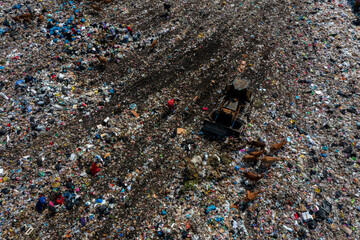 Aerial view of a vast, sprawling landfill with a bulldozer compacting waste and animals scavenging,...