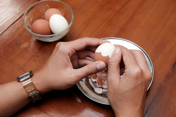 Close up of a man's hands peeling chicken boiled egg  on the kitchen table, prepares breakfast at home, health care and food concept. Copy space