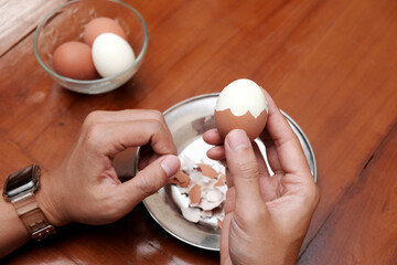 Close up of a man's hands peeling chicken boiled egg  on the kitchen table, prepares breakfast at home, health care and food concept. Copy space