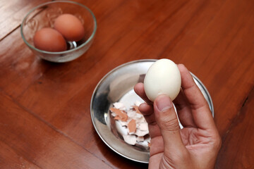 Close up of a man's hands holding chicken boiled egg  on the kitchen table, prepares breakfast at...