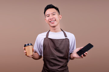 Smiling Young Barista Man Holding Coffee Cup And Smartphone Looking At Camera
