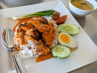 Authentic Thai dish called Moo Deng which translates as Red Pork. Plated with rice, boiled egg, cucumber, spring onion and a clear broth.