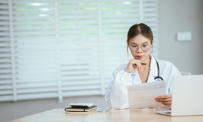 A concerned female doctor in a white lab coat and stethoscope holds her forehead, reading a...