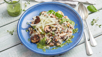 Oat risotto with vegetables, mushrooms and green pesto on blue plate