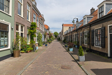 A quaint, brick-paved street in Delft, lined with charming traditional Dutch houses, vibrant potted...