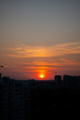 Sunset over city skyline with residential buildings and construction cranes. Urban landscape at dusk. Cityscape and sunset concept