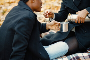 Loving black couple have a picnic in autumn park and drink a tea