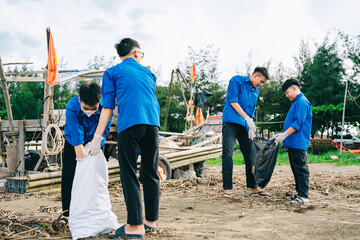 Group of volunteers in blue shirts cleaning up a beach while picking up trash near a fishing boat...