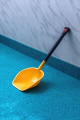 Yellow Plastic Shovel on Blue Floor Against Marble Wall