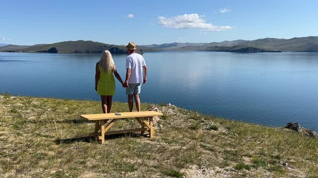 A couple enjoys a romantic walk on a sunny day, holding hands and sharing laughter by the seaside. - Powered by Adobe