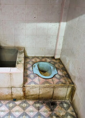 Traditional squat toilet in tiled bathroom with geometric patterned floor and aged ceramic fixtures